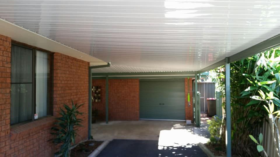 A Brick House With A Carport And A Green Garage Door — Boambee Home Improvements in Nambucca Heads, NSW