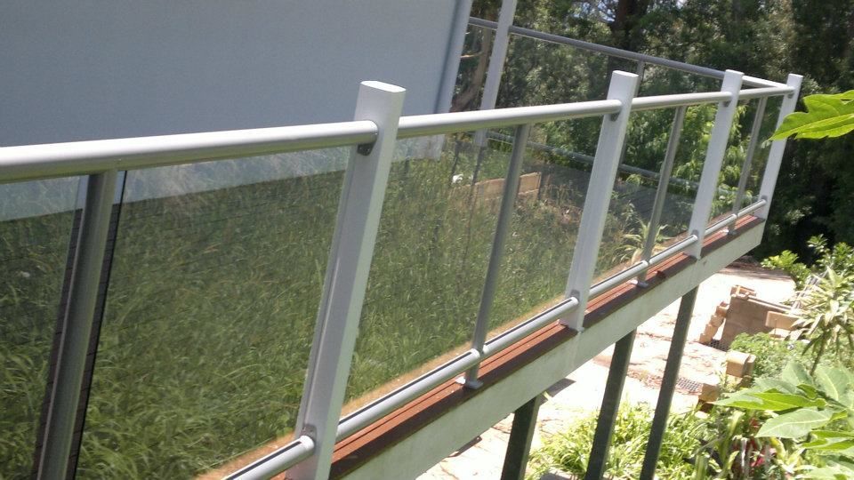 A Balcony With A Glass Railing Is Surrounded By Trees And Grass  — Boambee Home Improvements in Coffs Harbour, NSW