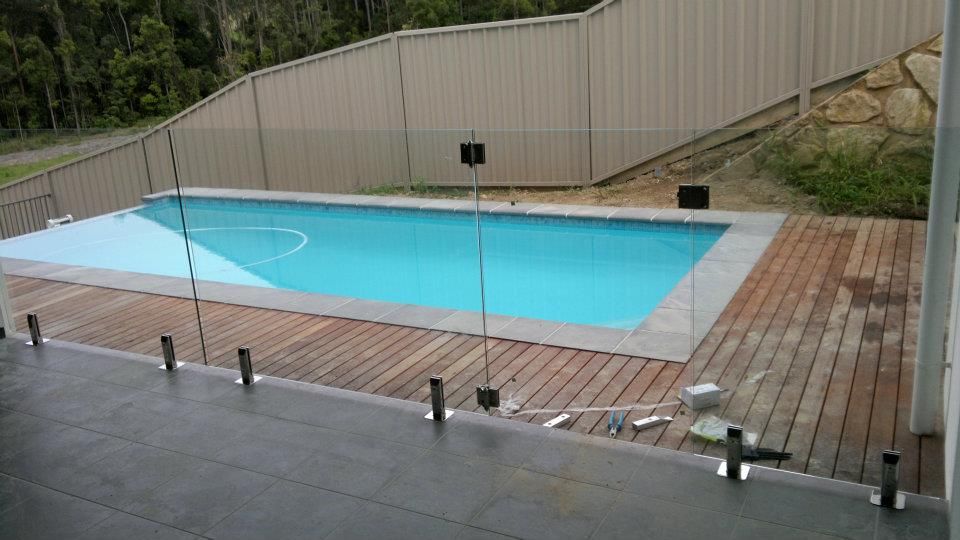 A Large Swimming Pool With A Glass Fence Around It — Boambee Home Improvements in Coffs Harbour, NSW