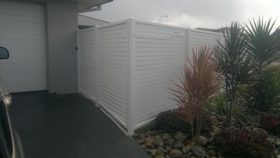 A White Fence Is Surrounded By Plants And Rocks In Front Of A House — Boambee Home Improvements in Coffs Harbour, NSW