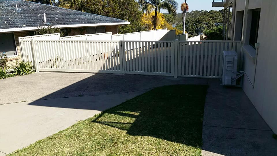 A White Fence Surrounds A Driveway In Front Of A House — Boambee Home Improvements in Coffs Harbour, NSW