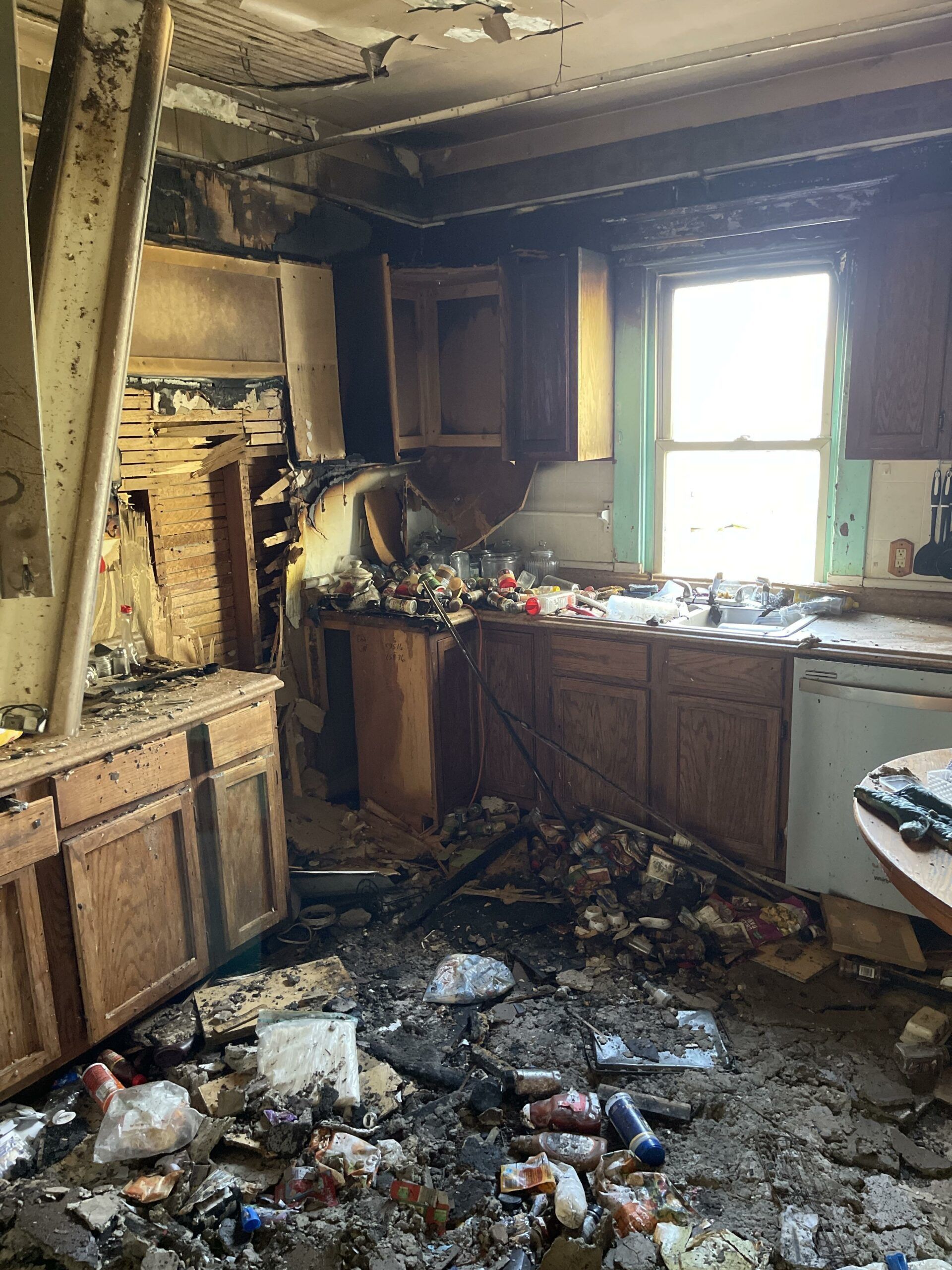 A kitchen with a lot of trash on the floor and a window.