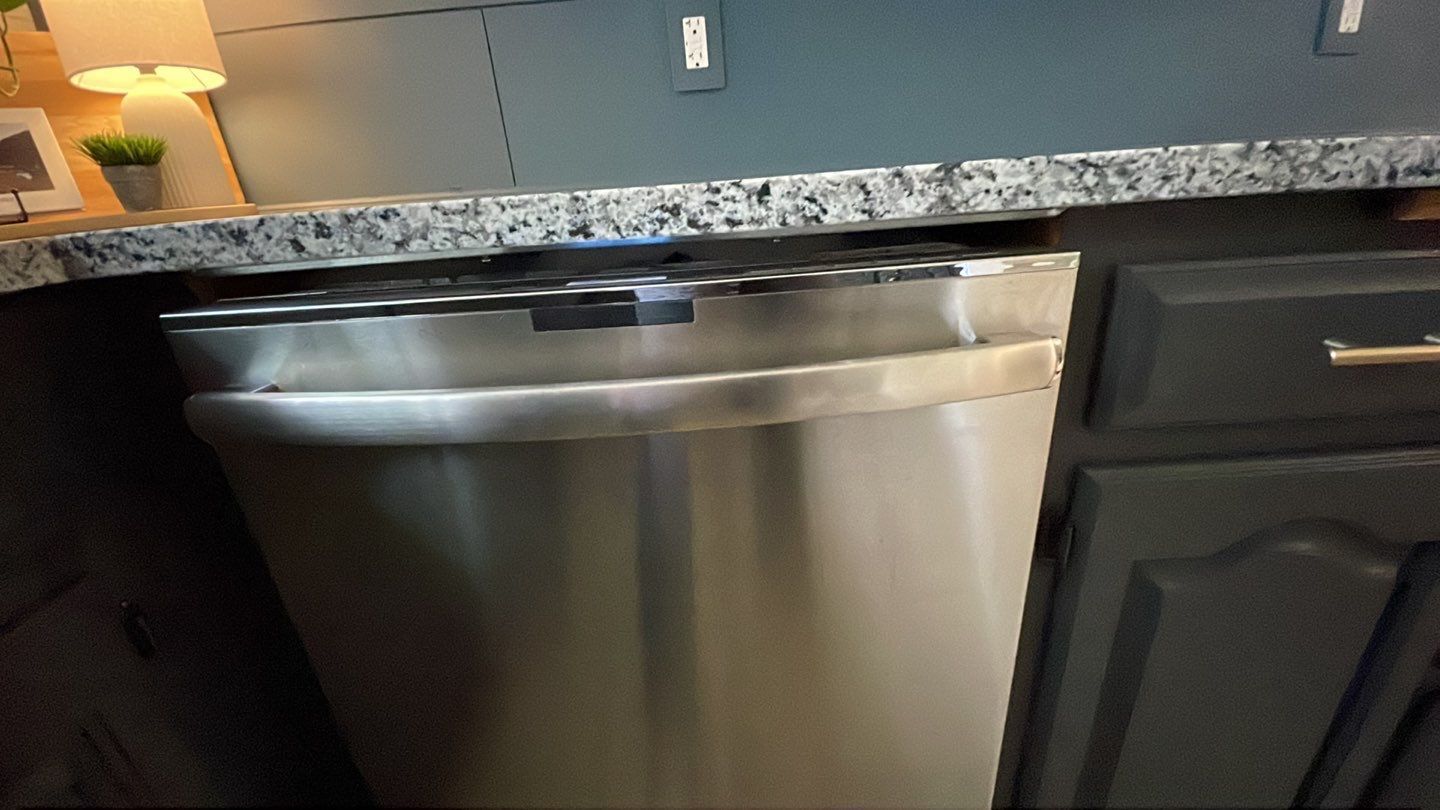 A stainless steel dishwasher is sitting under a granite counter top in a kitchen.