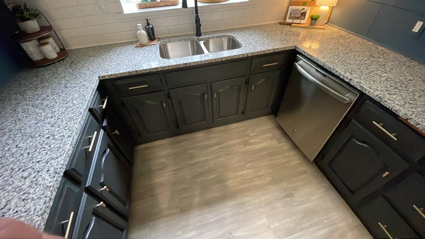 A kitchen with granite counter tops , black cabinets , a sink and a dishwasher.