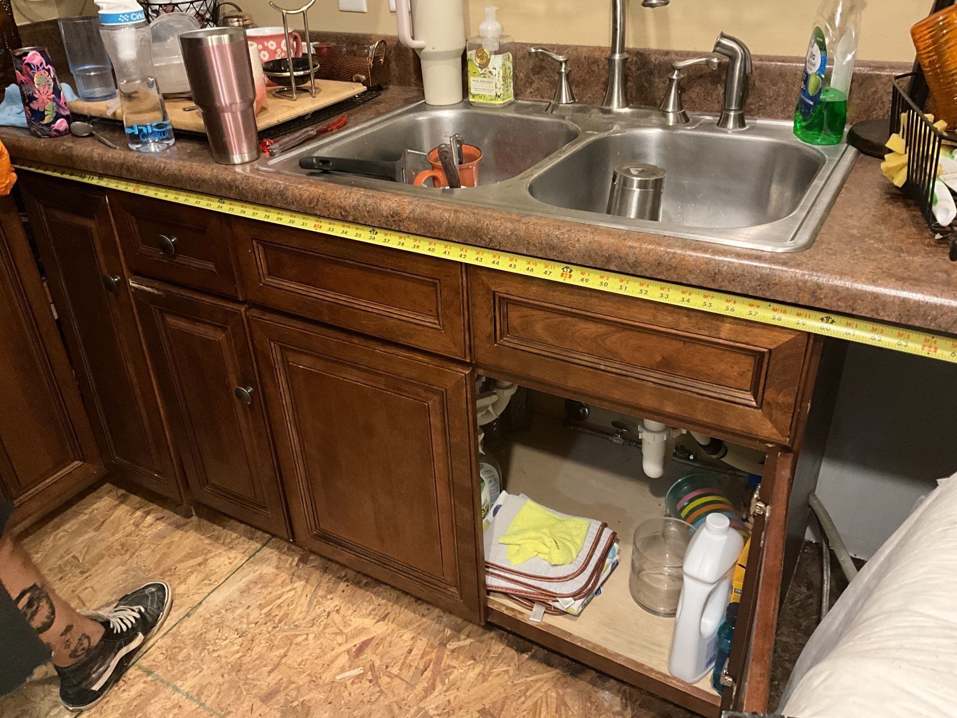 A person is measuring a kitchen sink with a tape measure.