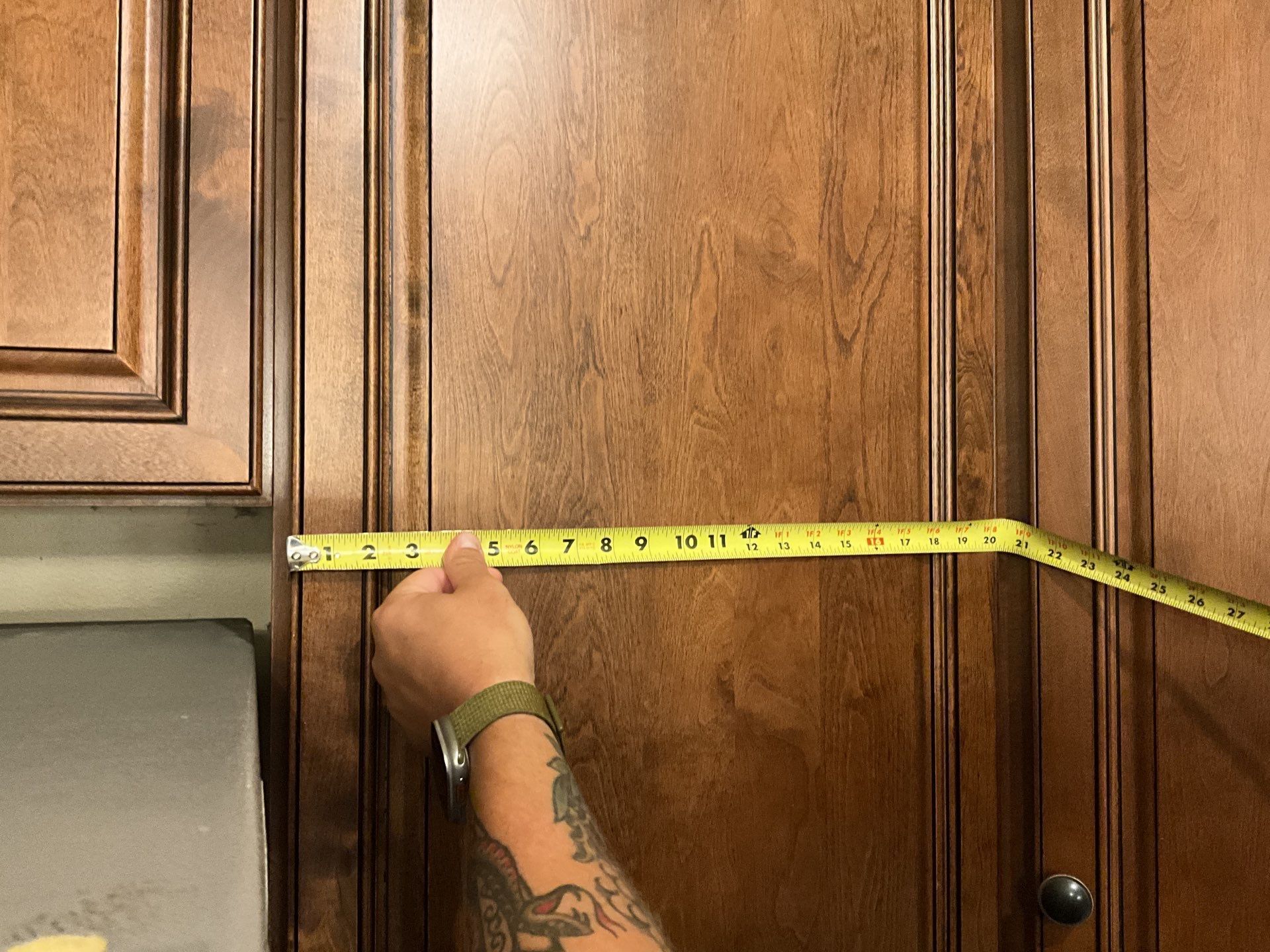 A person is measuring a cabinet door with a tape measure.