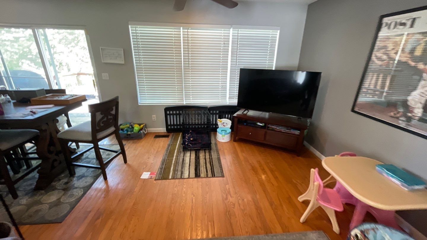 A living room with hardwood floors , a flat screen tv , a table and chairs.
