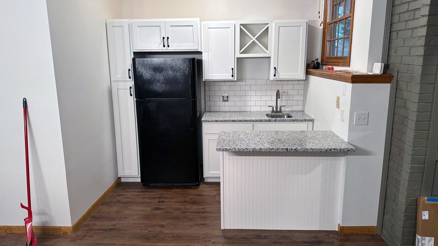 A kitchen with white cabinets , a black refrigerator , a sink , and a mop.