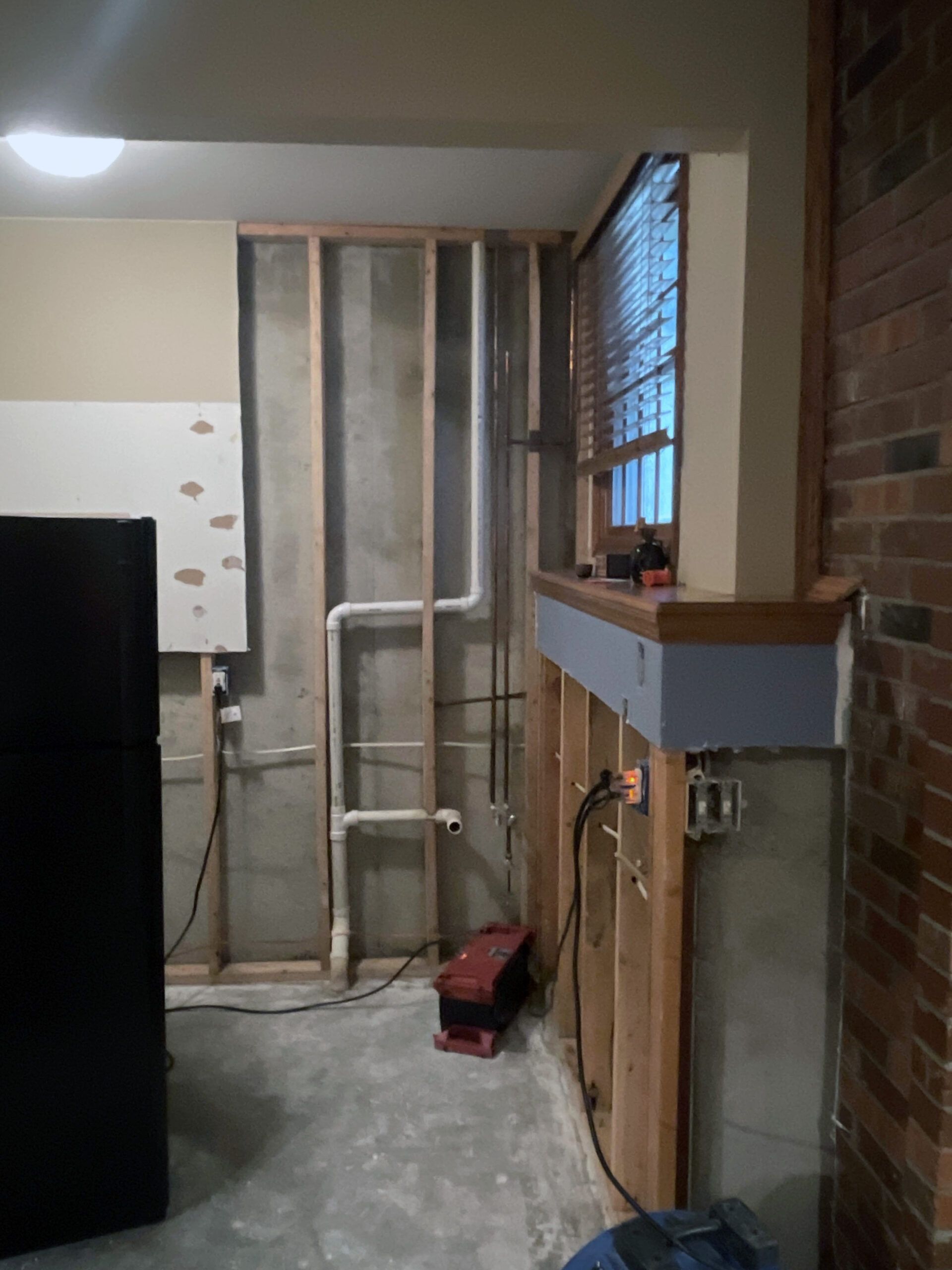 A room with a brick wall and a black refrigerator