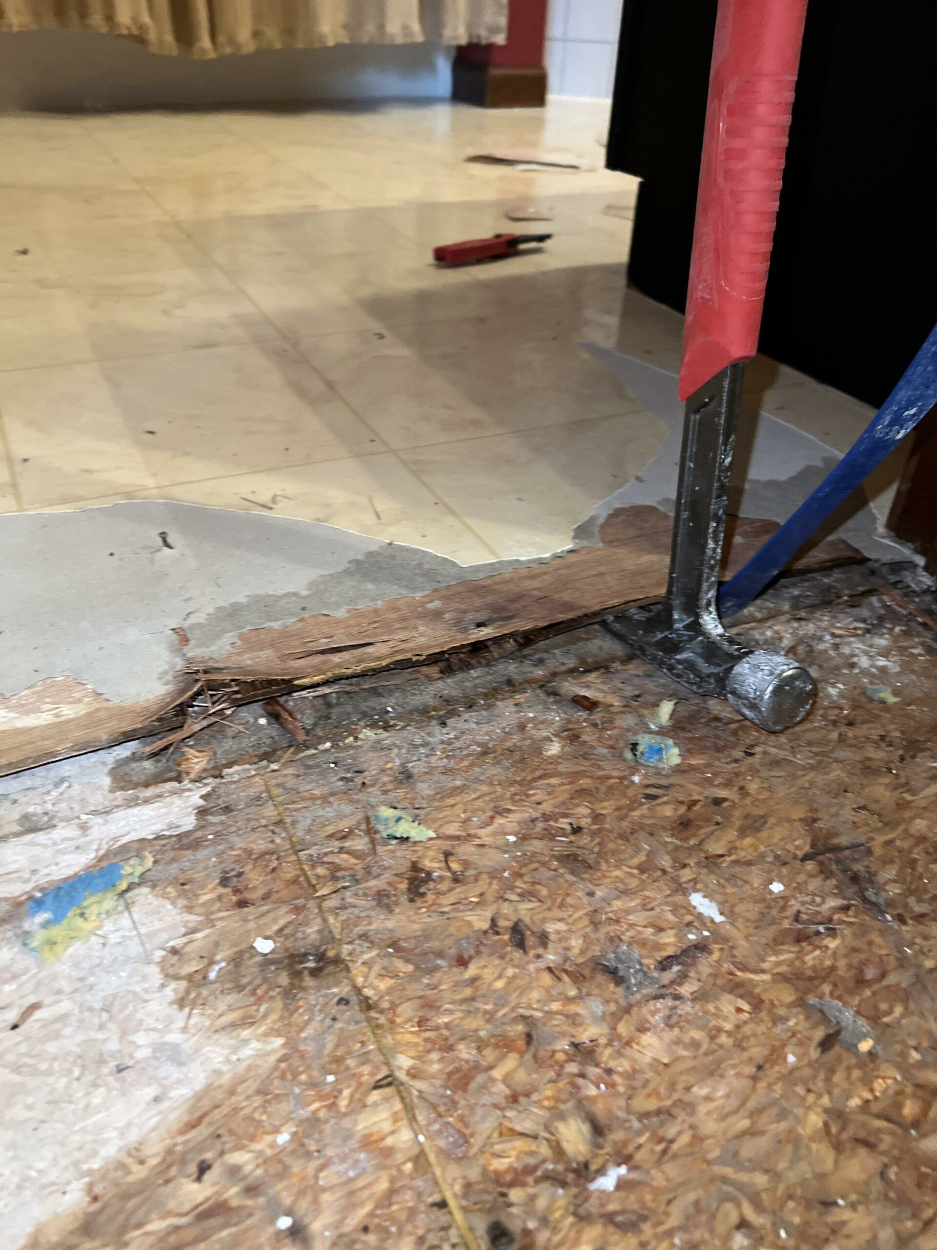 A hammer is being used to remove a piece of wood from the floor.