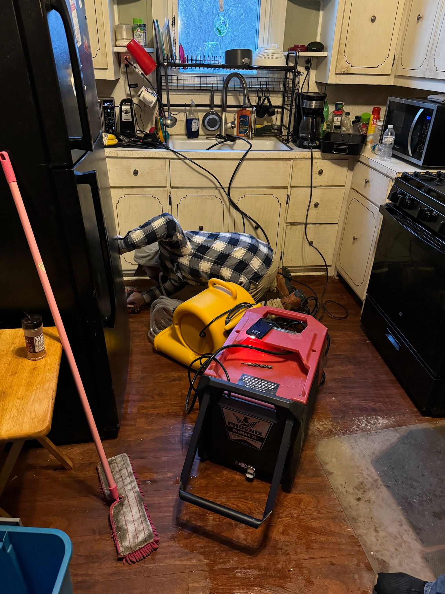 A kitchen with a lot of appliances and a mop on the floor.