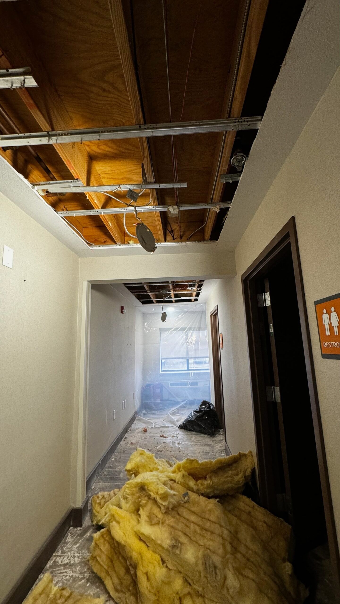 A hallway with a ceiling that has been damaged and a pile of insulation on the floor.