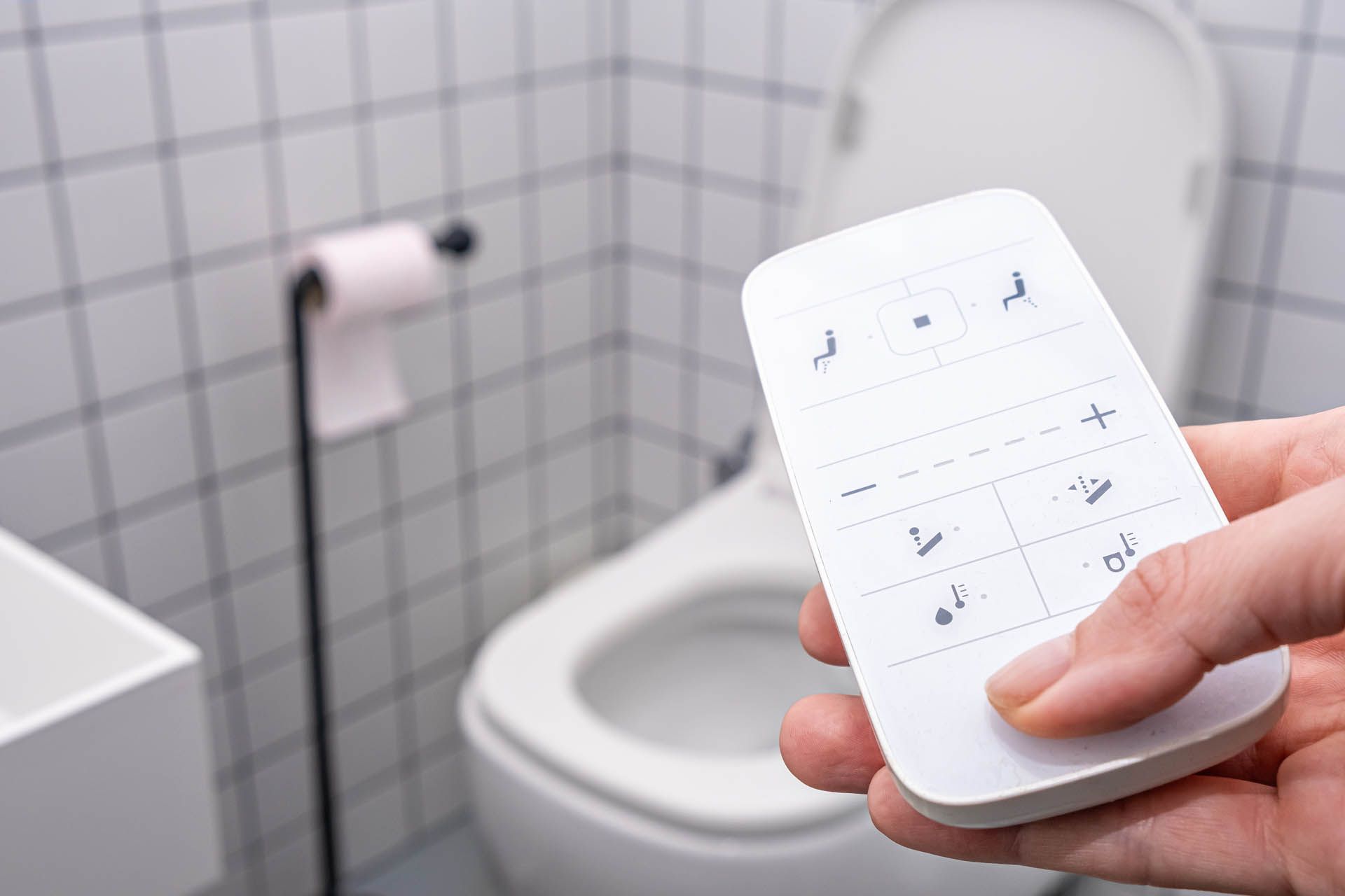 a person is holding a remote control in a bathroom in front of a toilet .