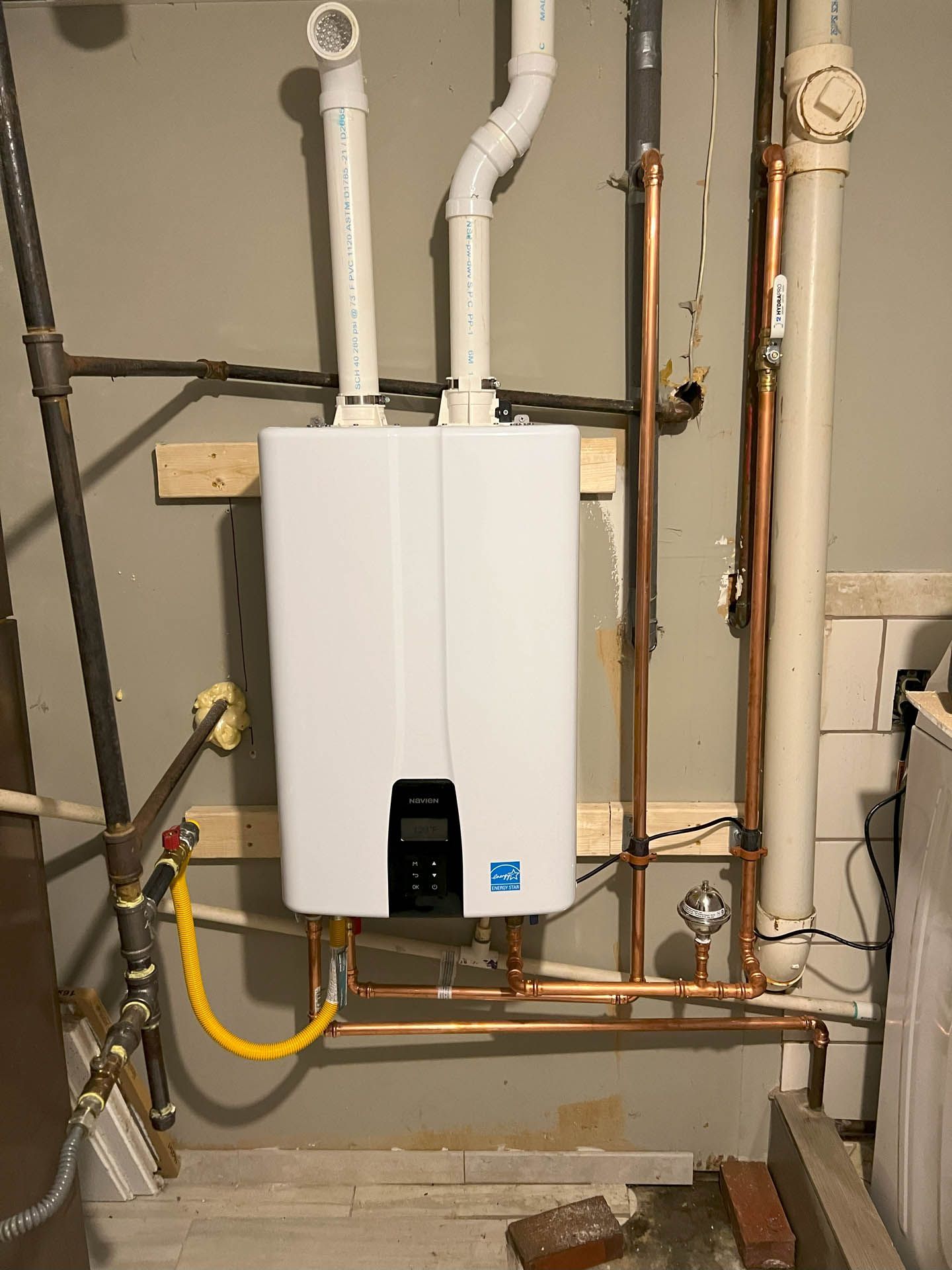 A white water heater is hanging on a wall next to copper pipes.