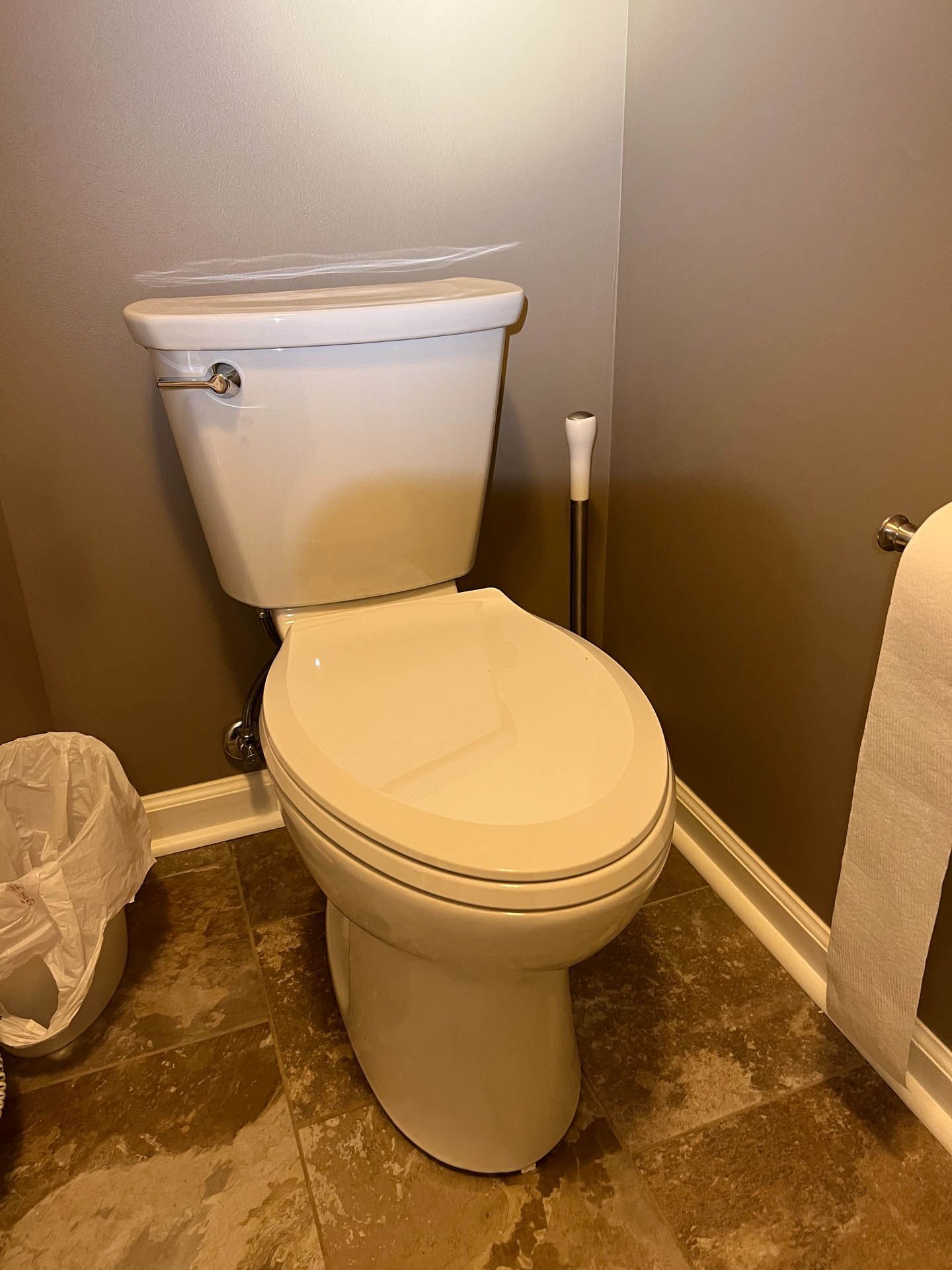 A white toilet is sitting in a bathroom next to a trash can.