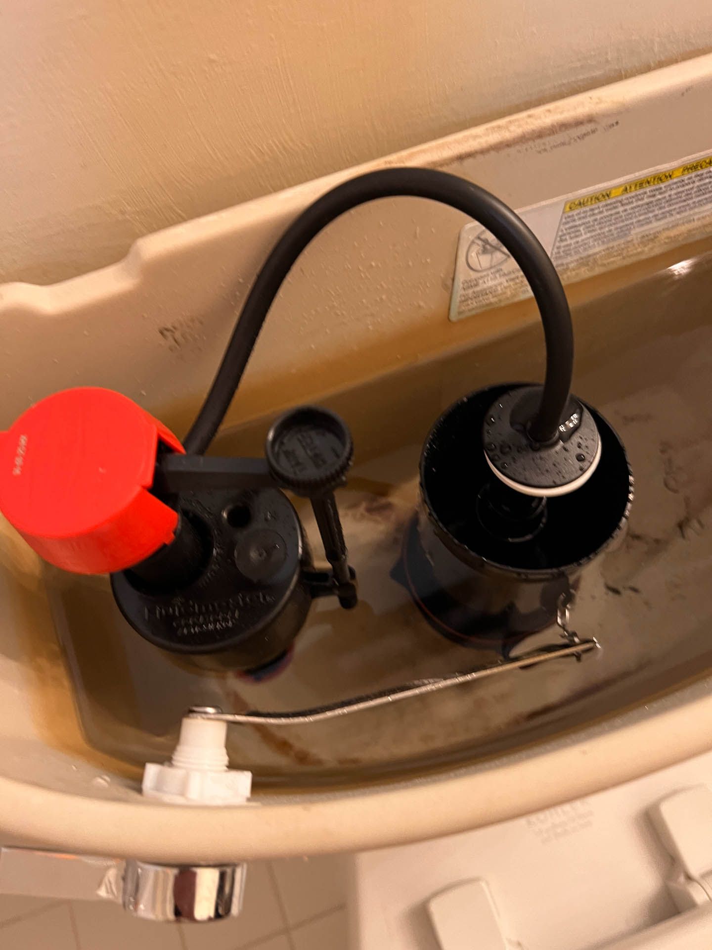 A close up of a toilet tank with a red handle