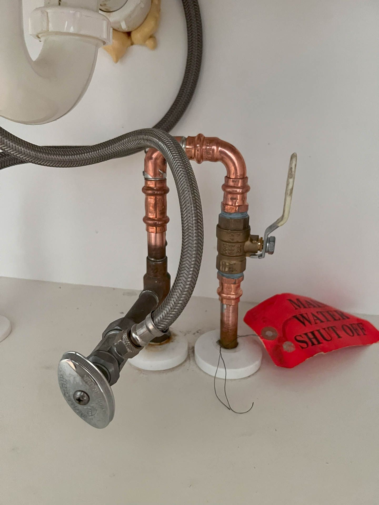 Copper pipes under a sink with a red tag that says water shut off