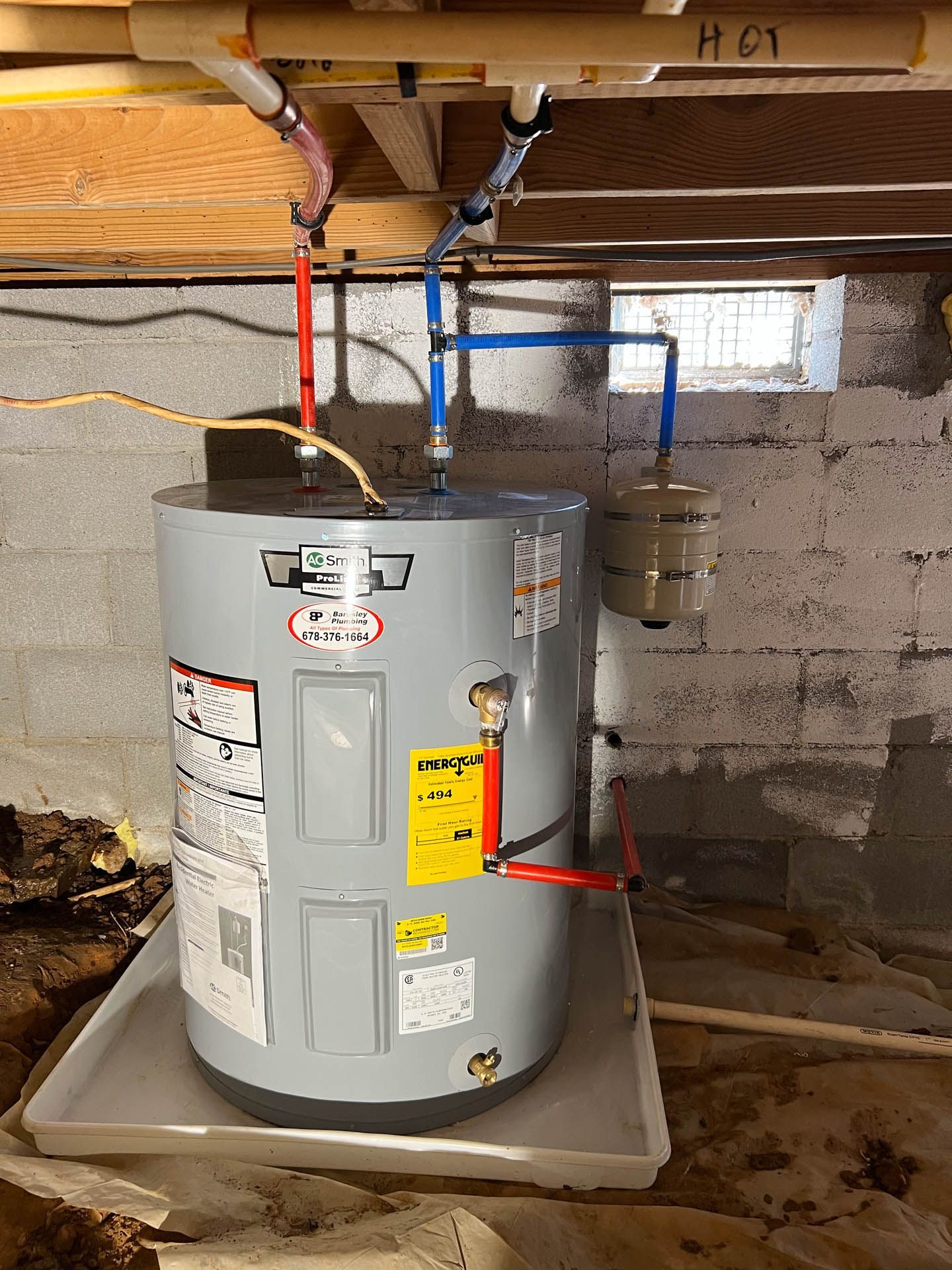 A water heater is sitting on top of a tray in a basement.