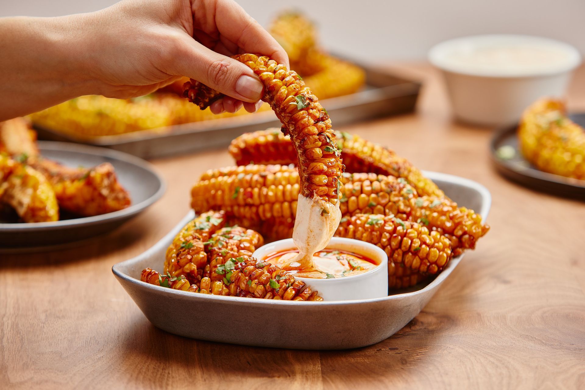 A person is dipping a piece of corn into a bowl of sauce.