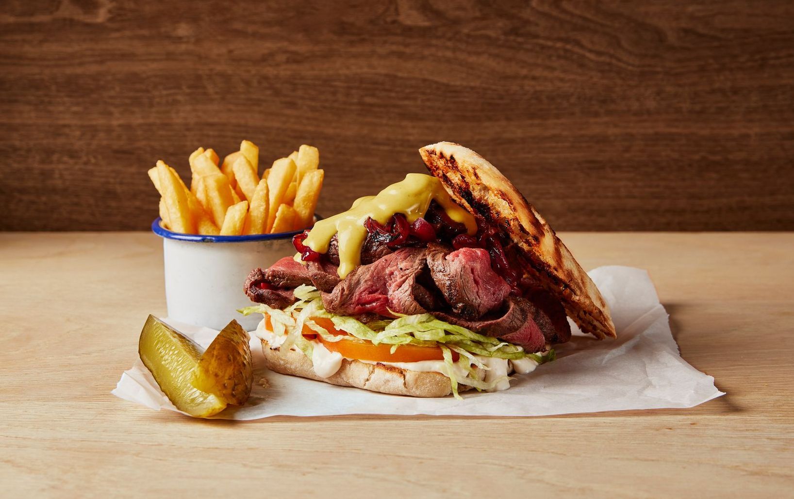 A sandwich with french fries and pickles on a wooden table.