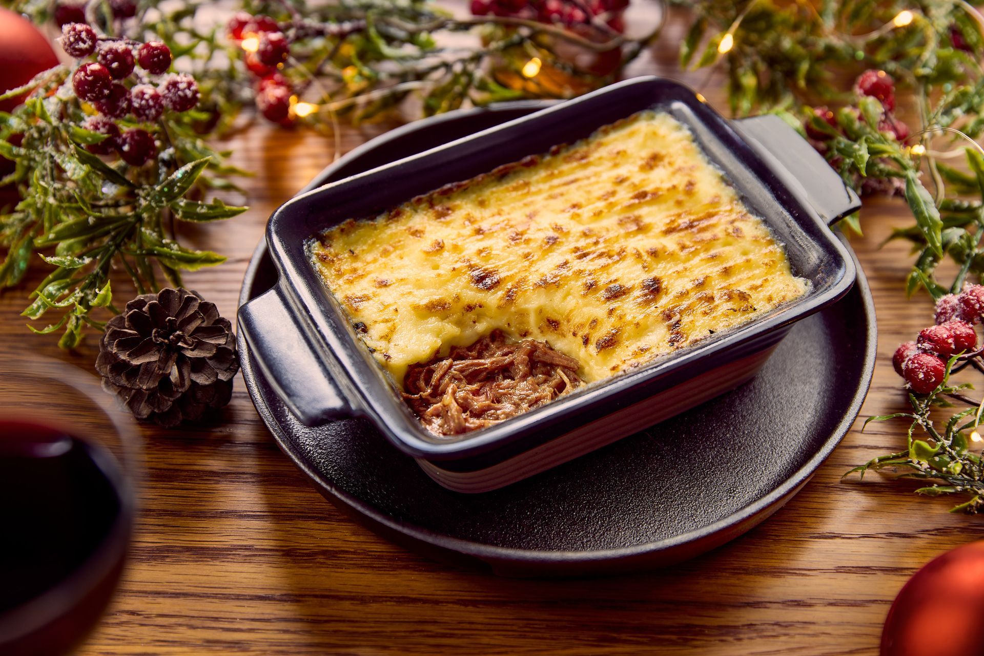 A casserole dish filled with food is on a plate on a wooden table.