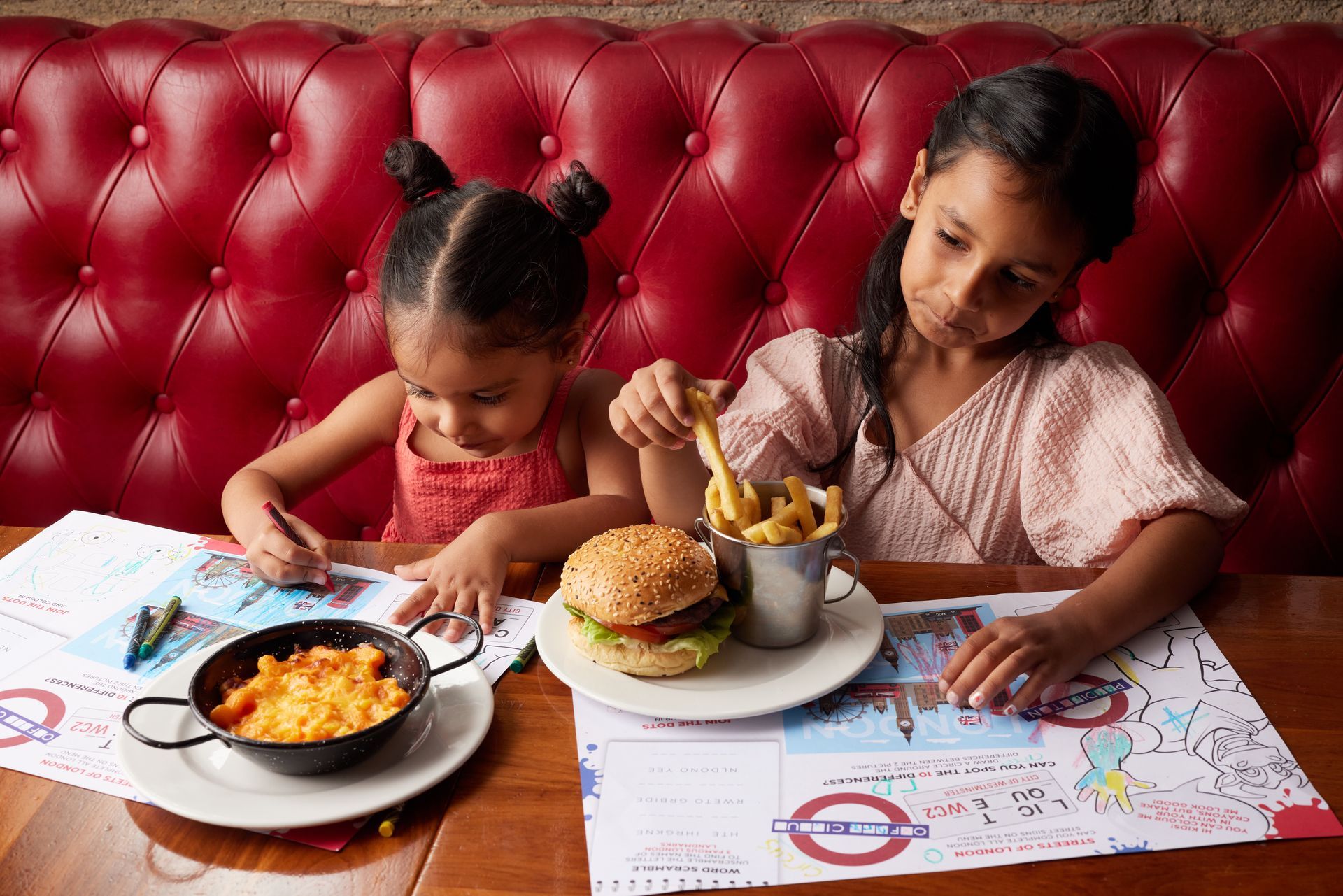 Two little girls are sitting at a table with plates of food.