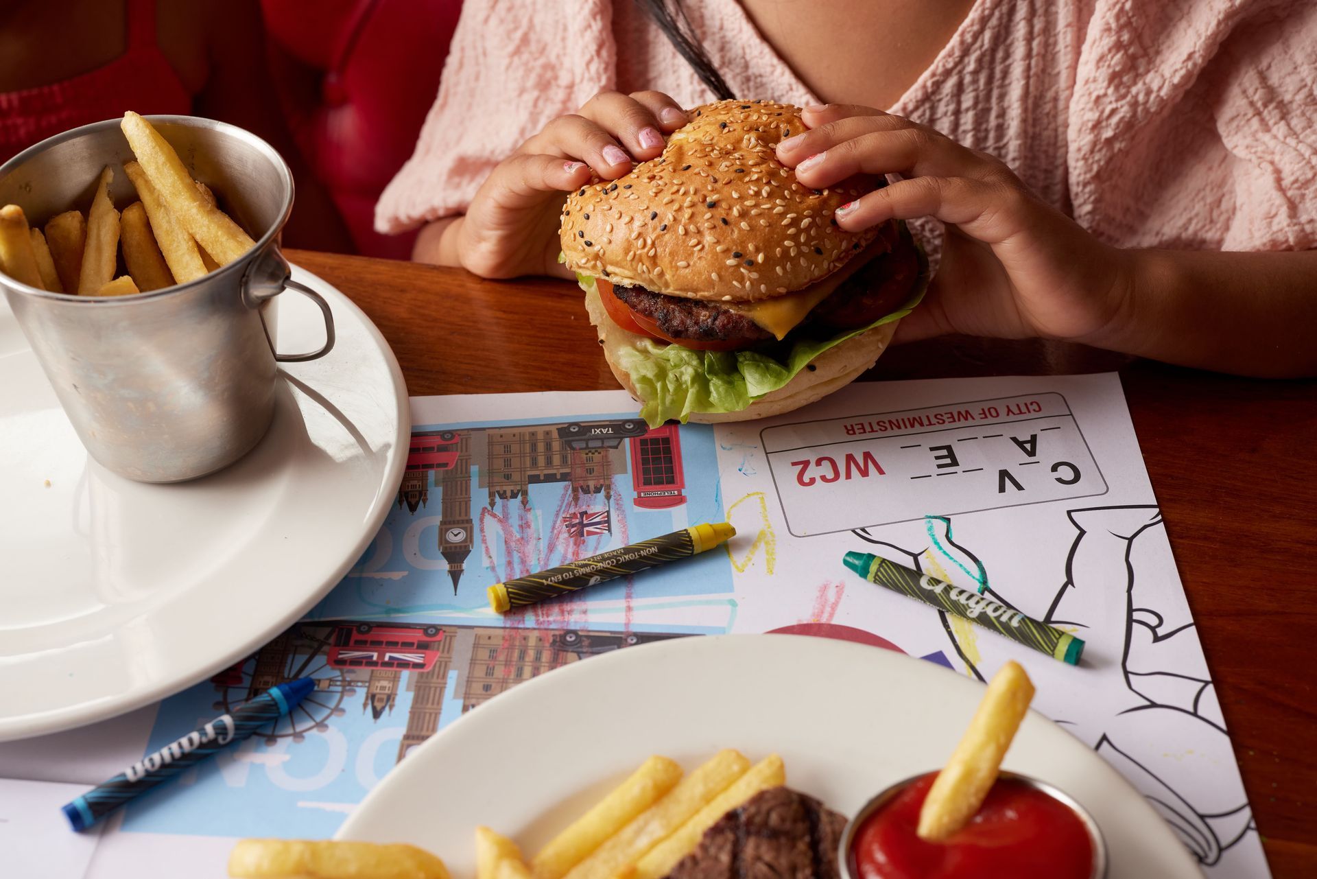 A child is sitting at a table eating a hamburger and french fries.