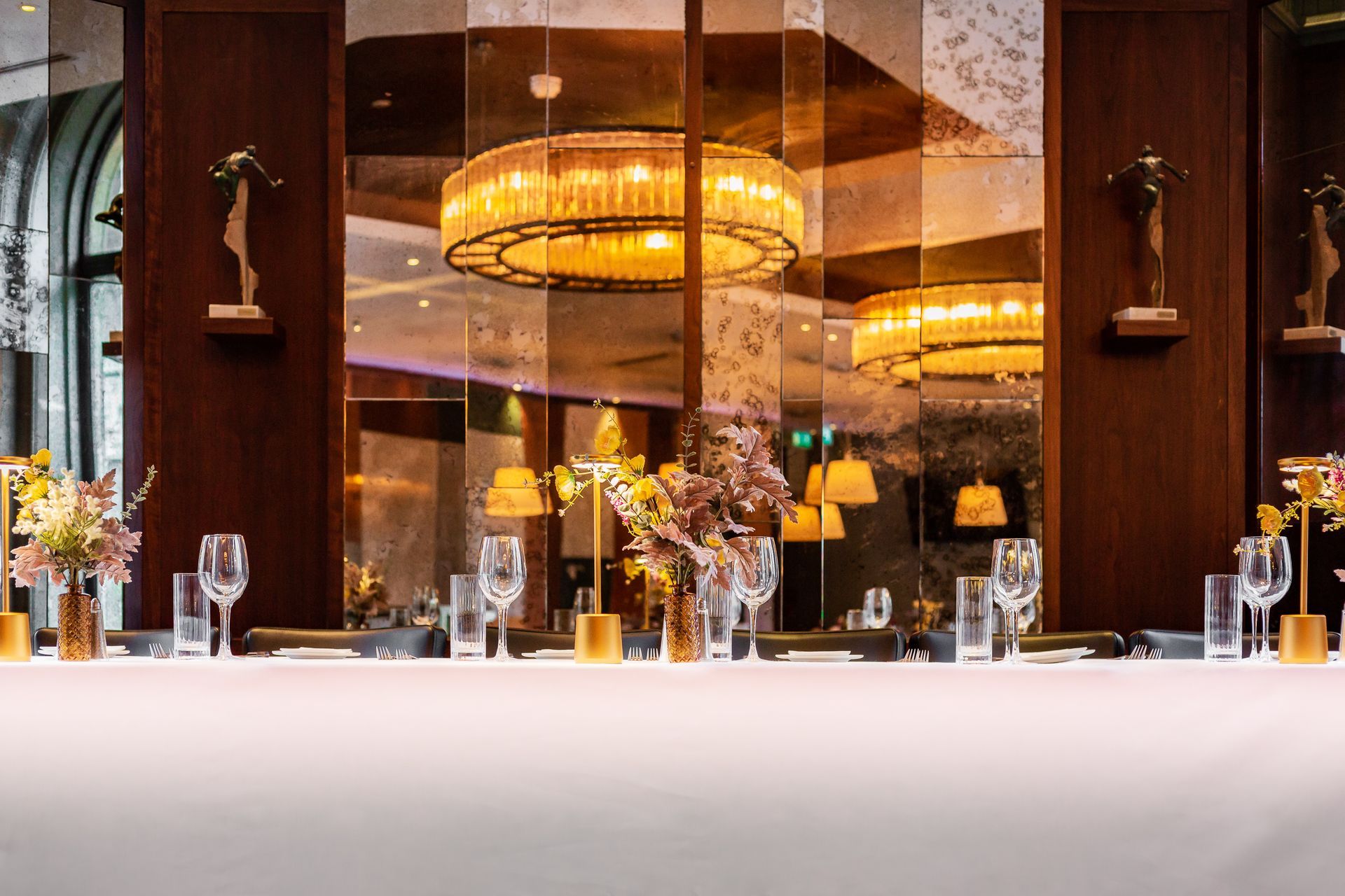 A long table in a restaurant with glasses and flowers on it.