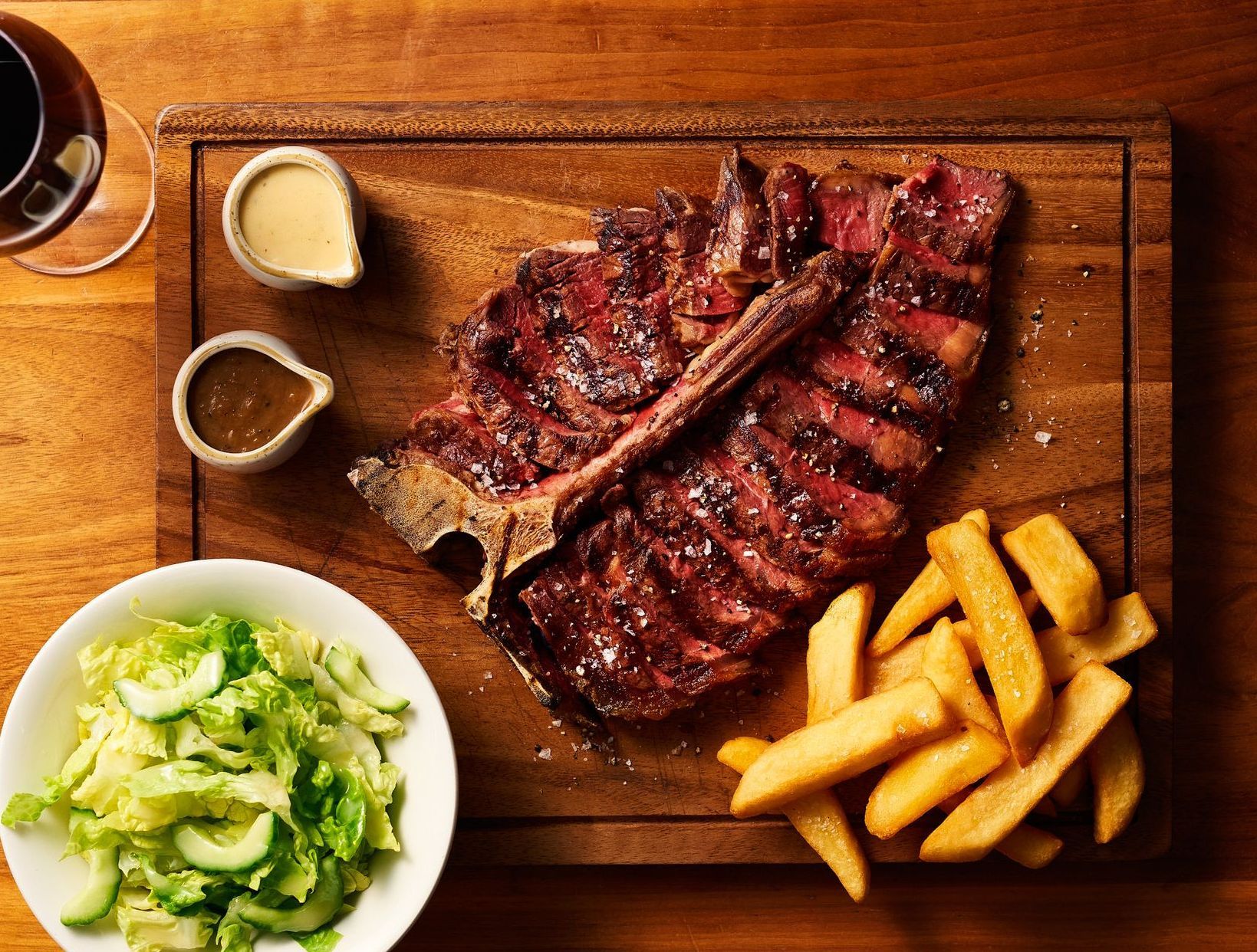 A large steak with french fries and a salad on a wooden cutting board.