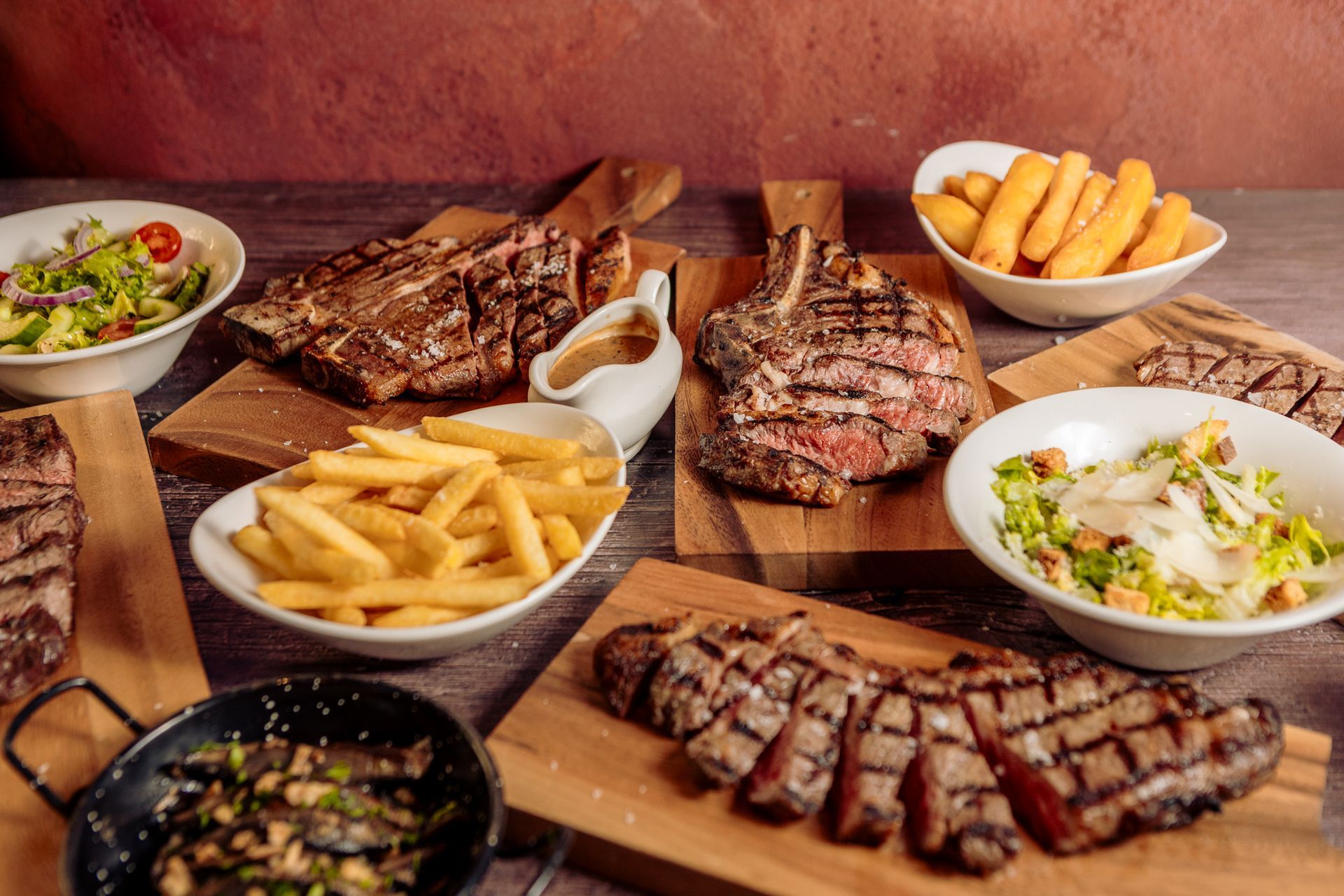 There are many different types of steaks and french fries on the table.