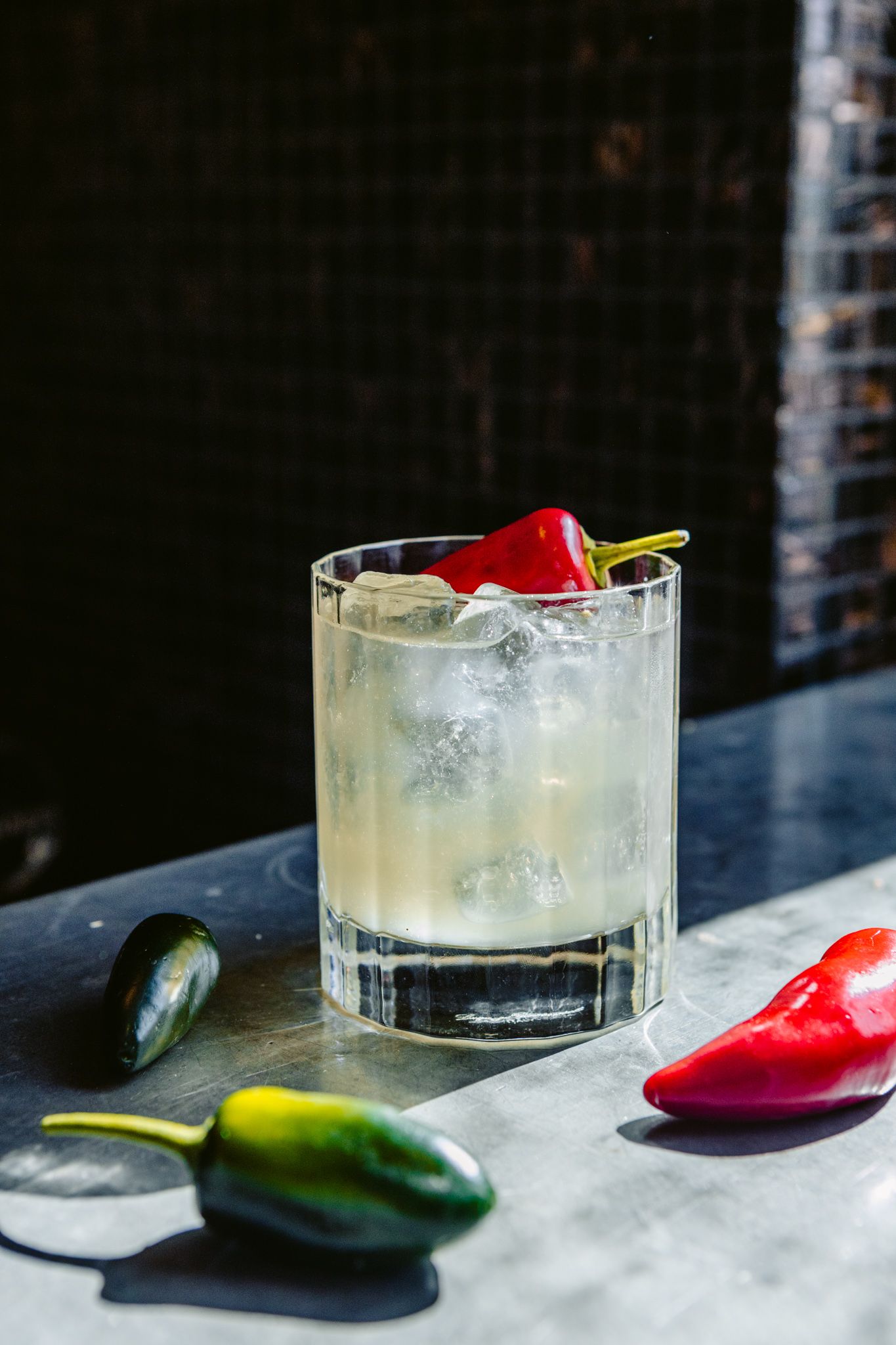 A close up of a drink in a glass on a table next to jalapenos.