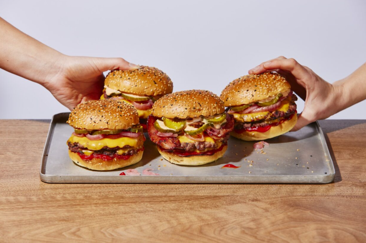 A bunch of hamburgers are sitting on a metal tray on a wooden table.