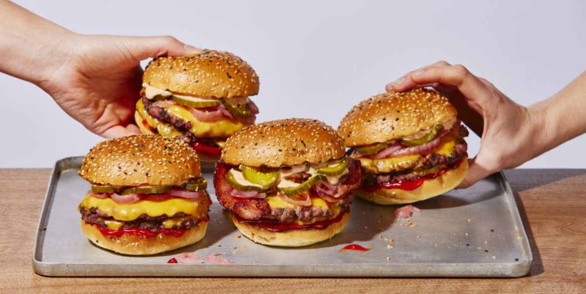 A person is holding three hamburgers on a tray.