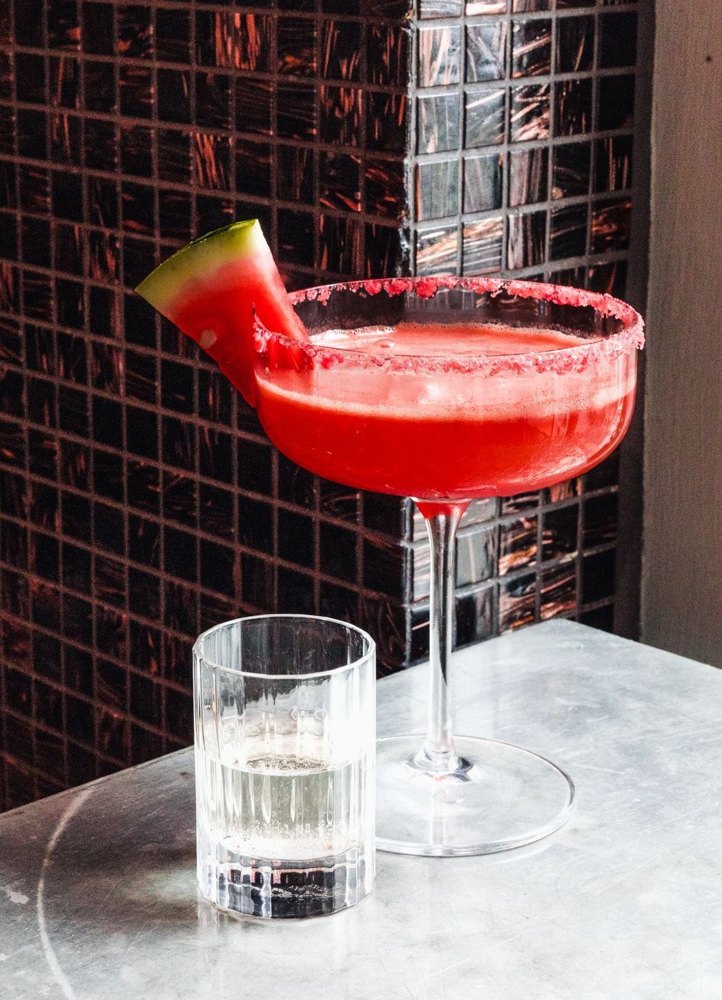 A watermelon margarita is sitting on a table next to a glass of water.