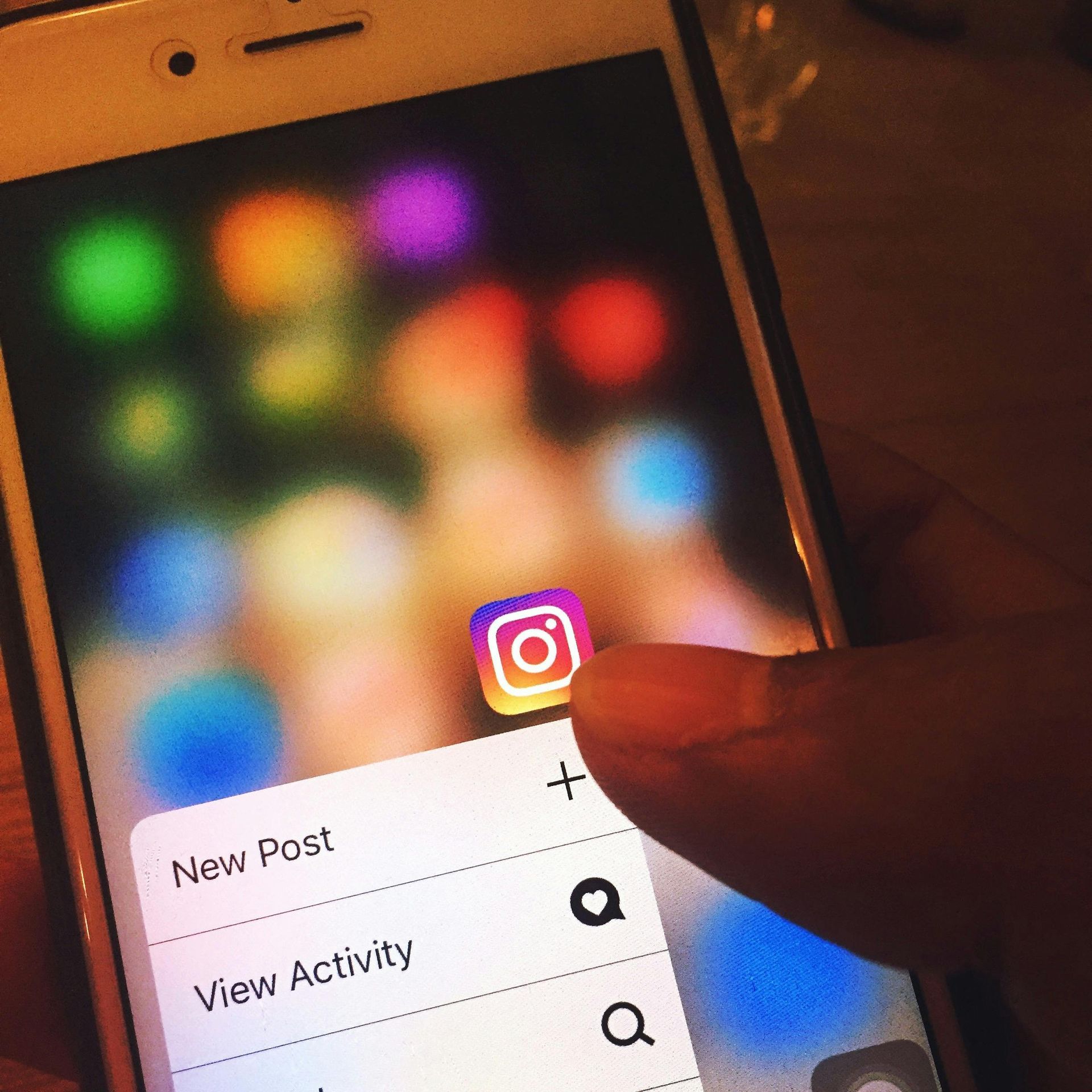 Phone screen with Instagram icon. Finger pressing on the icon to view options: New Post, View Activity.