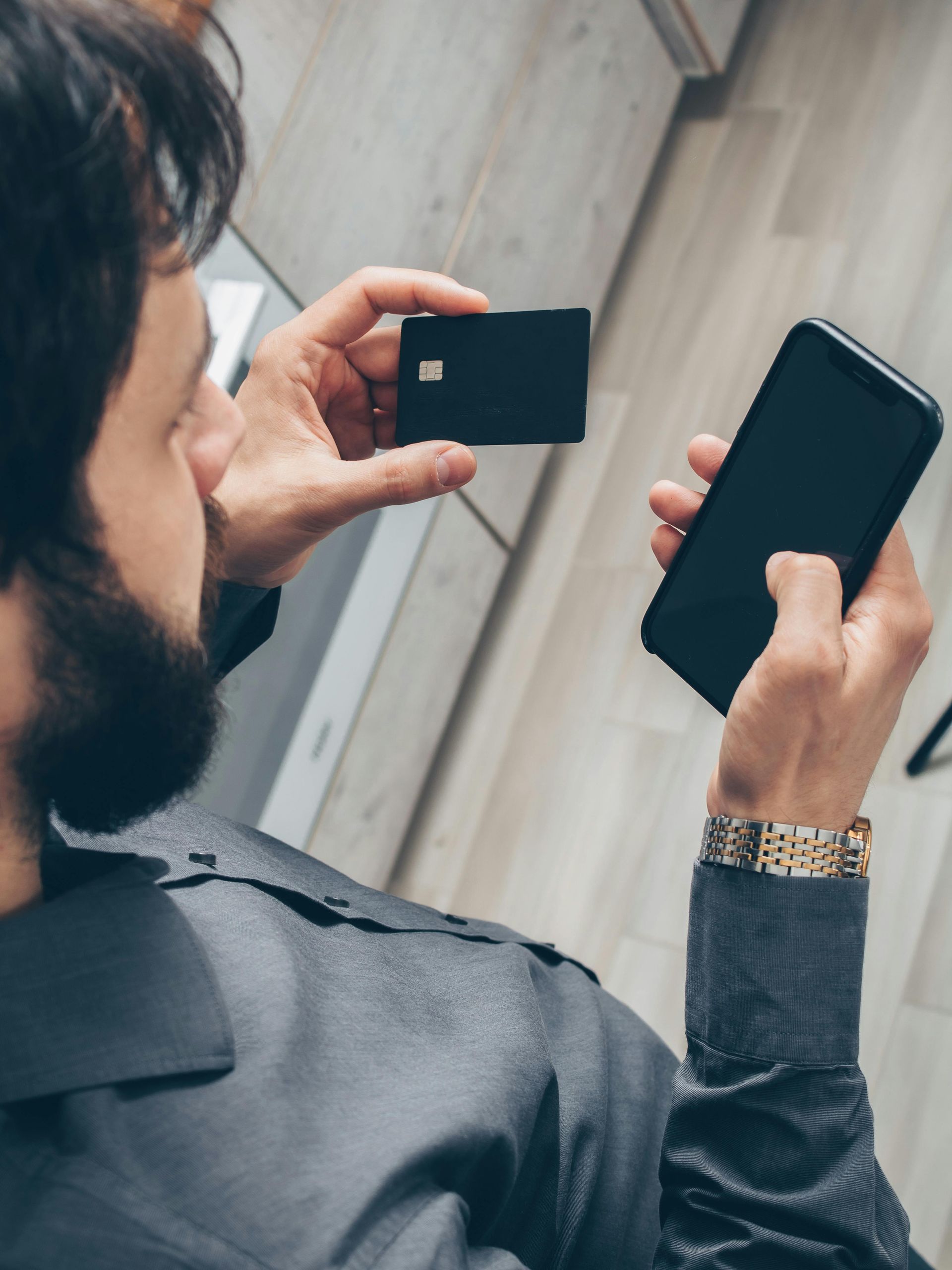 Person holding a black credit card and a smartphone, possibly making a payment.