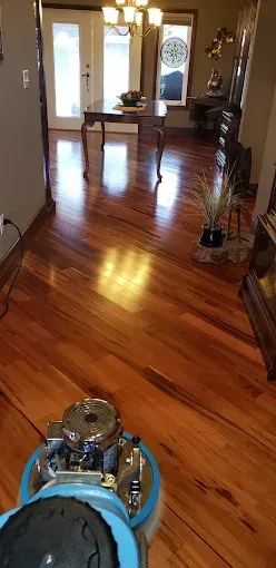 A person using a floor buffer on a polished wooden floor in a home.