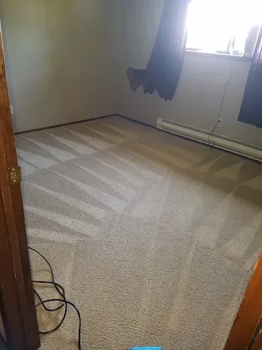 A freshly cleaned room with beige carpet, a window with dark curtains, and light beige walls.