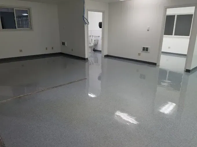 Empty room with glossy gray floor, white walls, doorways to a bathroom and another room with a window.