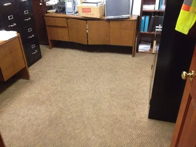 Office interior with beige carpet, wooden desk and cabinet. Some file cabinets and a monitor visible.