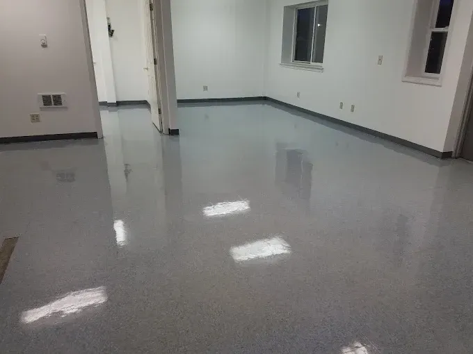 Empty room with shiny, speckled gray floor; white walls and trim; two windows.