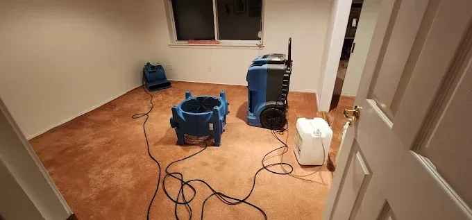Room with water damage, drying equipment deployed, brown carpet, white walls, open door.