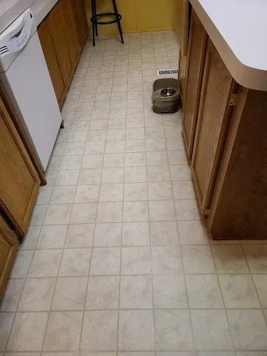 Kitchen with light-colored tile flooring, cabinets, and a white appliance. A pet bowl sits on the floor.
