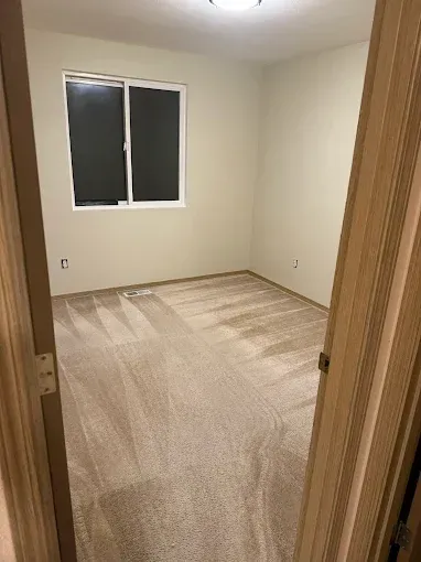 Empty room with beige walls, tan carpet, and a window. Doorway in foreground.