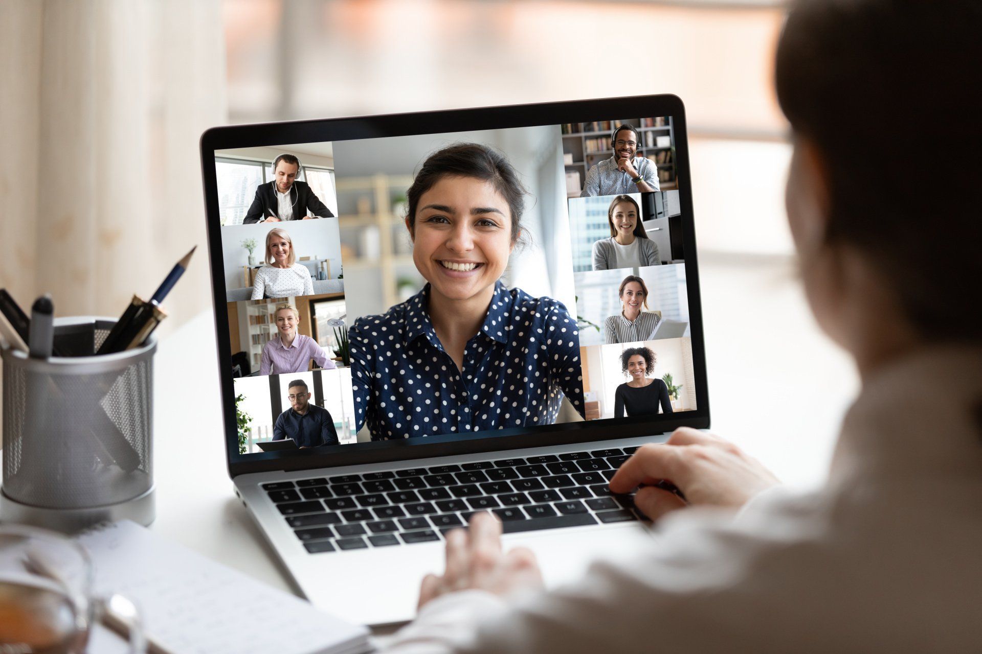 Person using laptop, engaged in a video conference with smiling participants on screen.