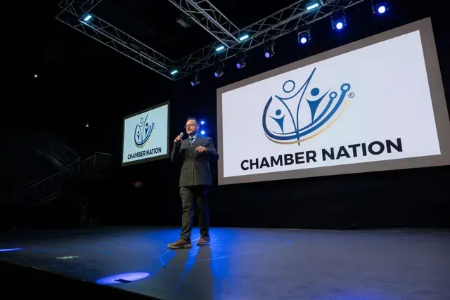 Man speaking on stage at Chamber Nation event, with logo on screens.