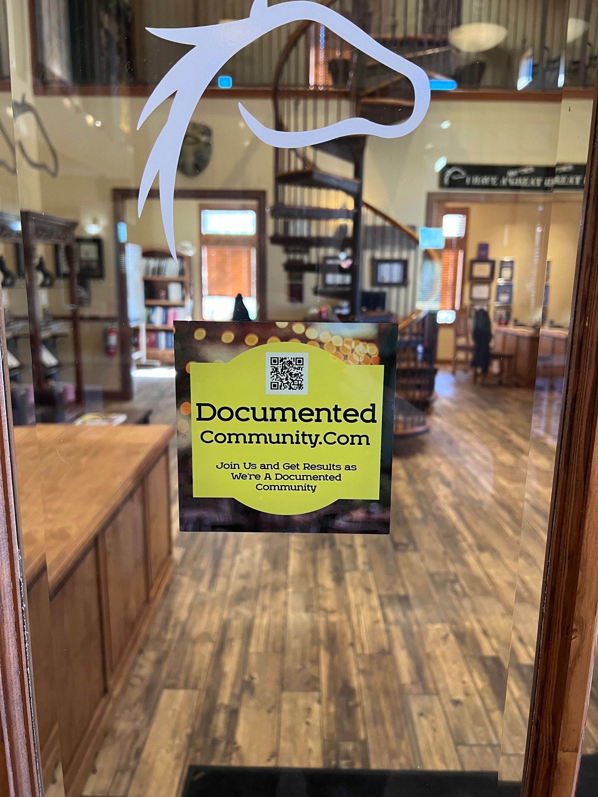 View into a store with a horse head logo. A sign reads “Documented Community Court.” Wooden floors and a spiral staircase are visible.