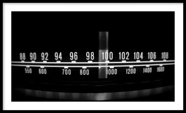 Close-up of a radio dial with frequency numbers, in black and white. The needle is set to 100 on the FM scale and 1000 on AM.