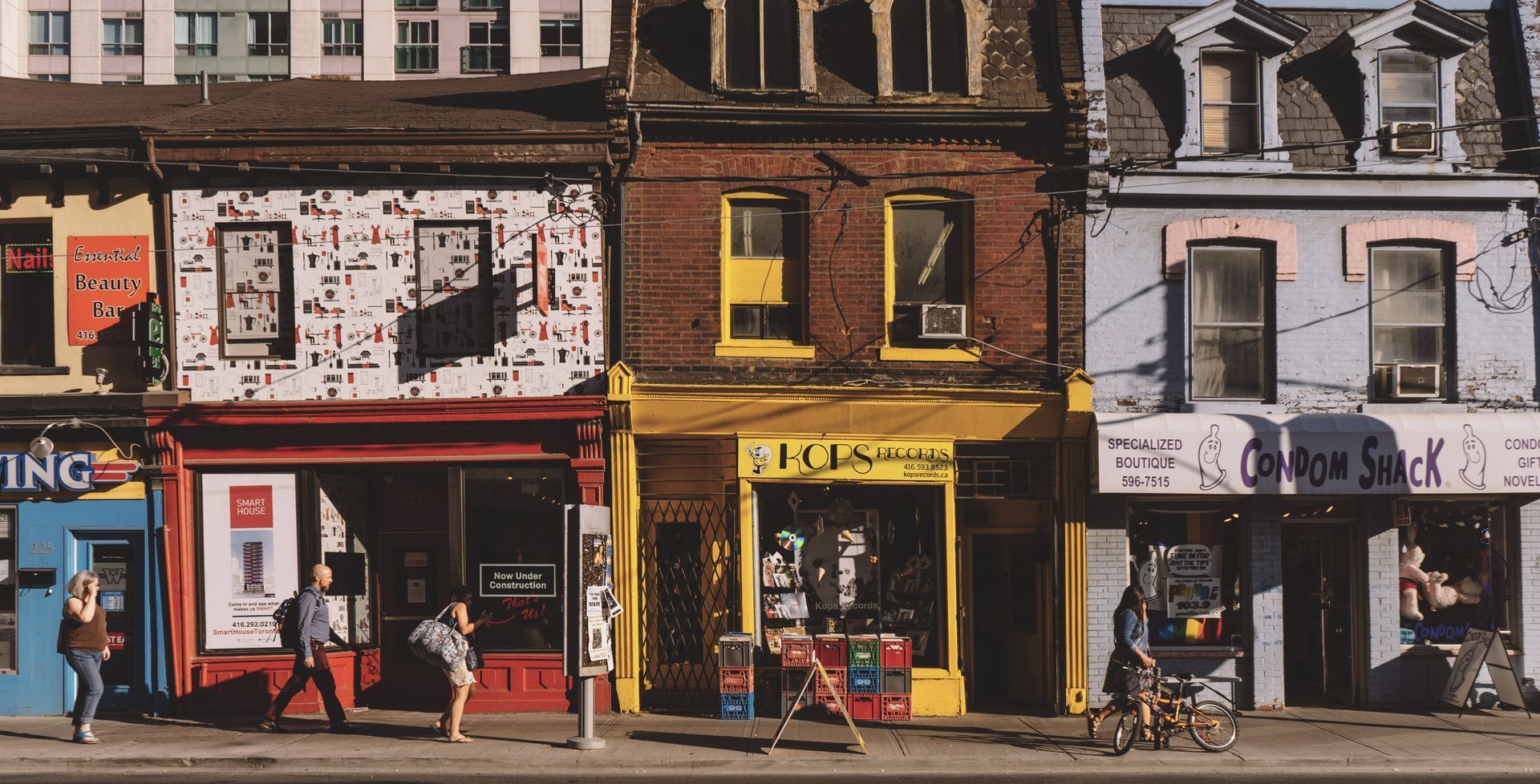 Row of colorful storefronts on a city street; pedestrians walk on the sidewalk.