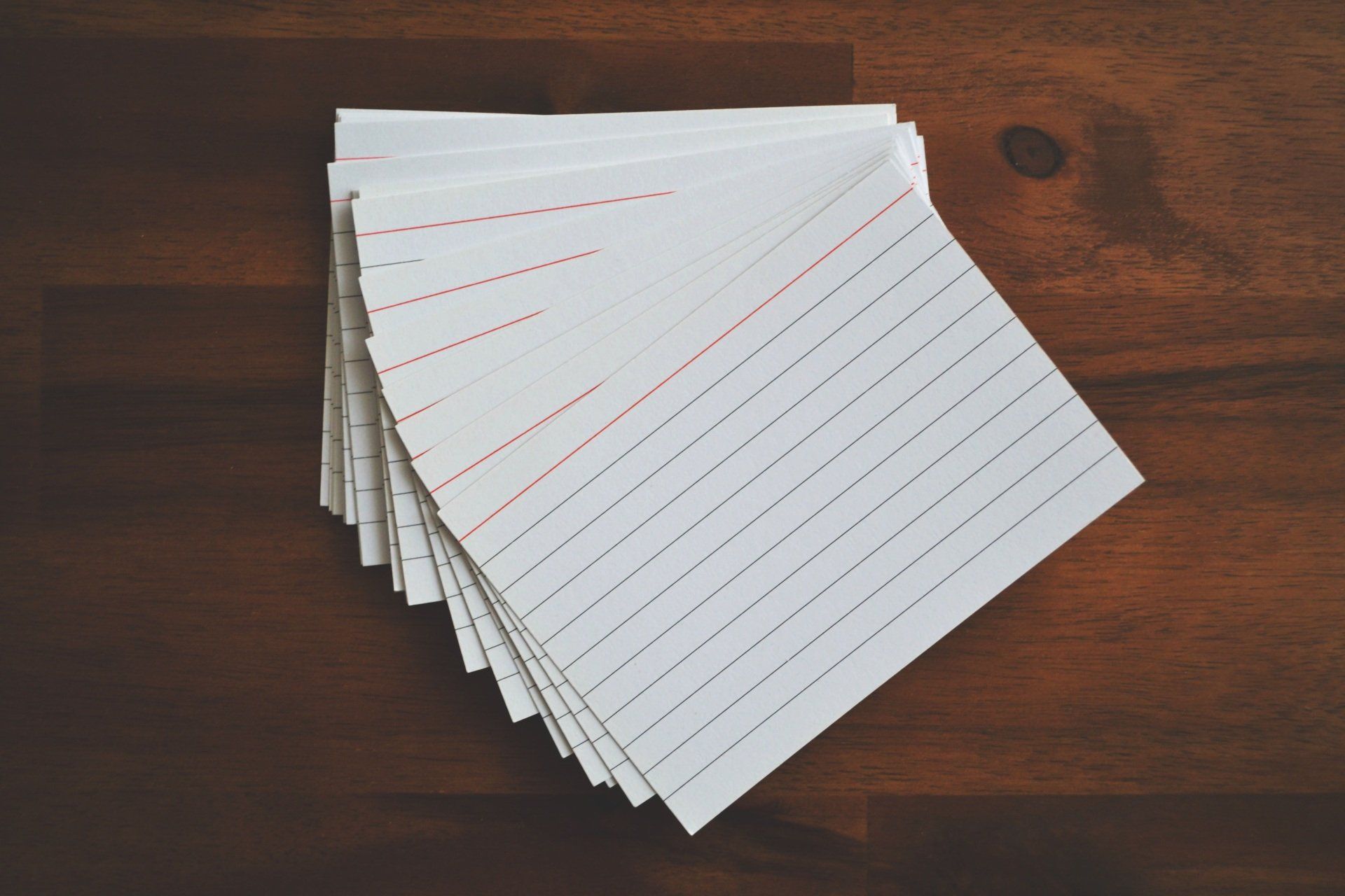 Stack of white, lined index cards on a dark wooden table.